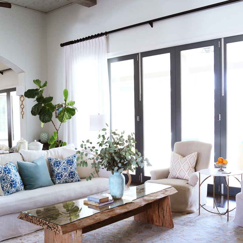 Bright living room in white with sofa, multiple throw pillows in blues and greens, a rough hewn wood live edge coffee table, and a cream  occasional chair
