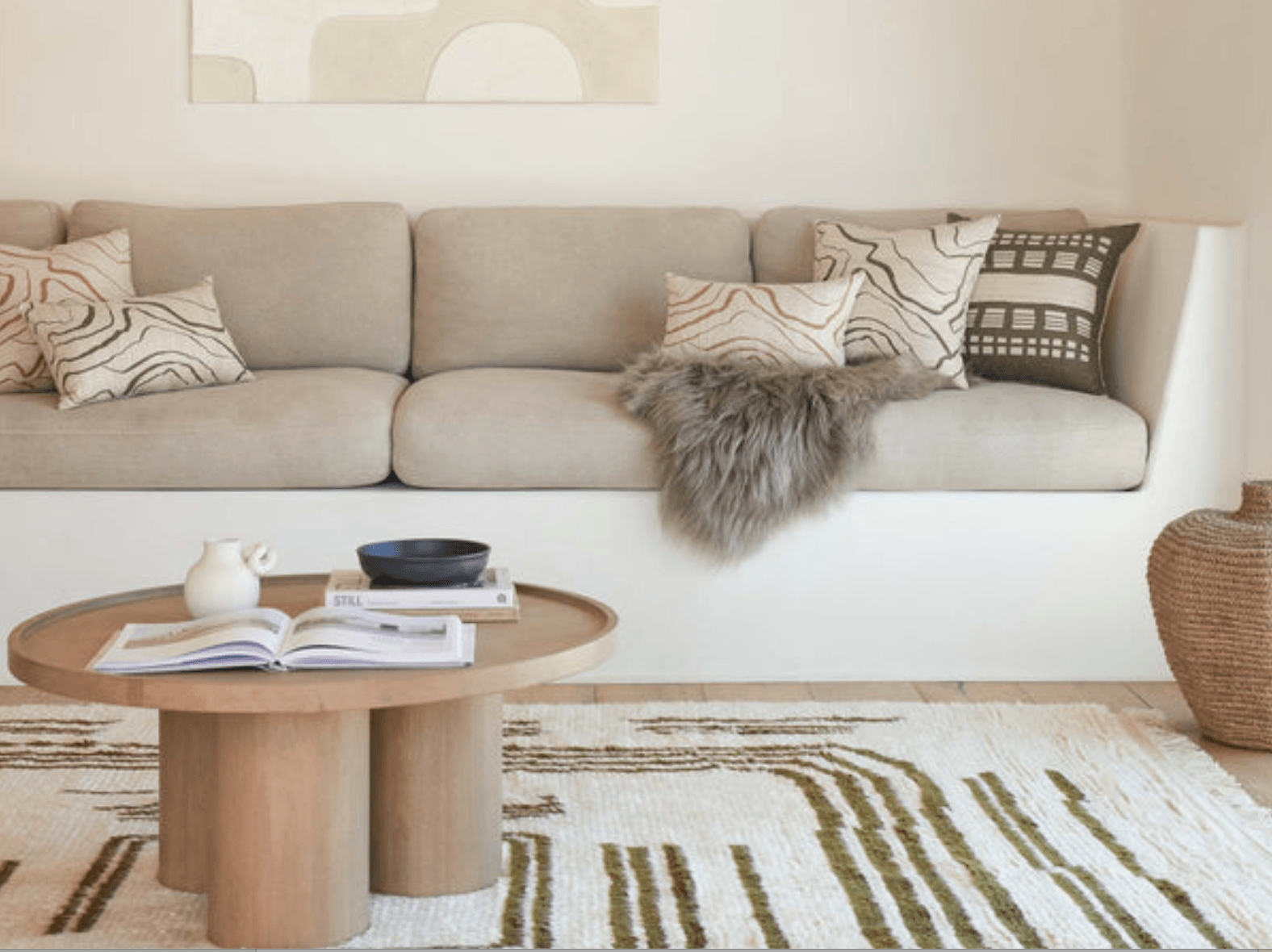 A neutral colored rug with a linear design by Elan Byrd is a great first buy, set in a living room with a cream and beige sofa and oval tray style coffee table 