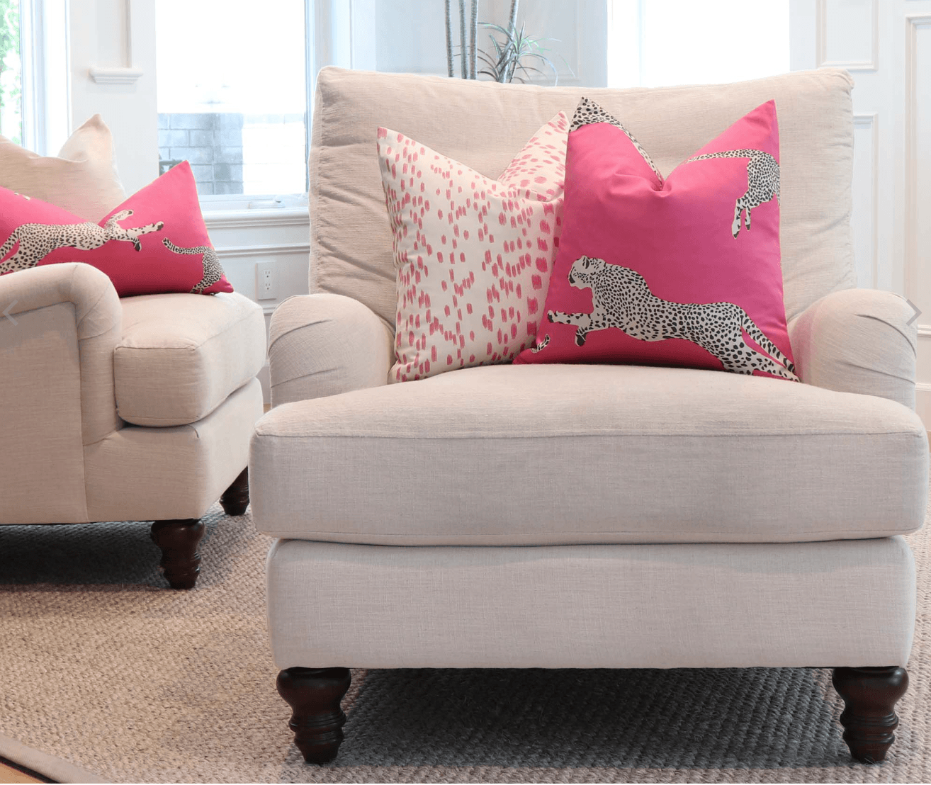 Cream armchairs with hot pink leopard and patterned throw pillows in a bright, modern living room.