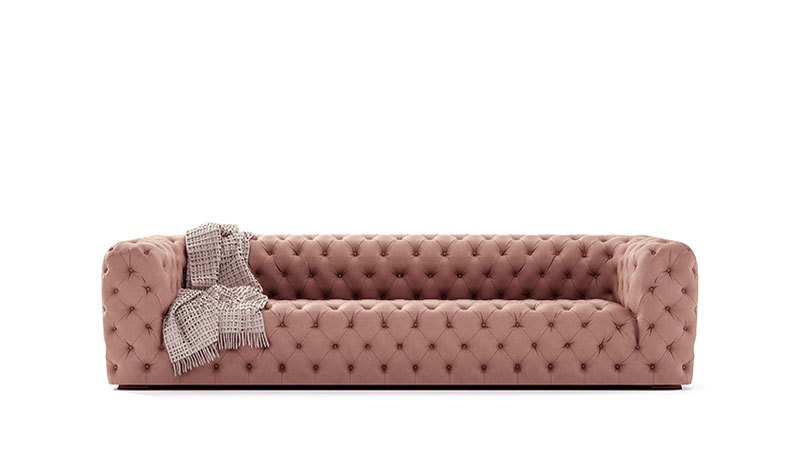 Blush pink tufted velvet sofa with low arms and back, styled with a soft woven throw.