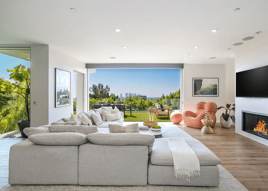 Modern living room with a large white sectional, striped accent chairs, a fireplace, and a view of the Los Angeles skyline.