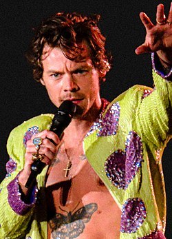 Harry Styles performing shirtless in a lime green and purple sequined jacket
