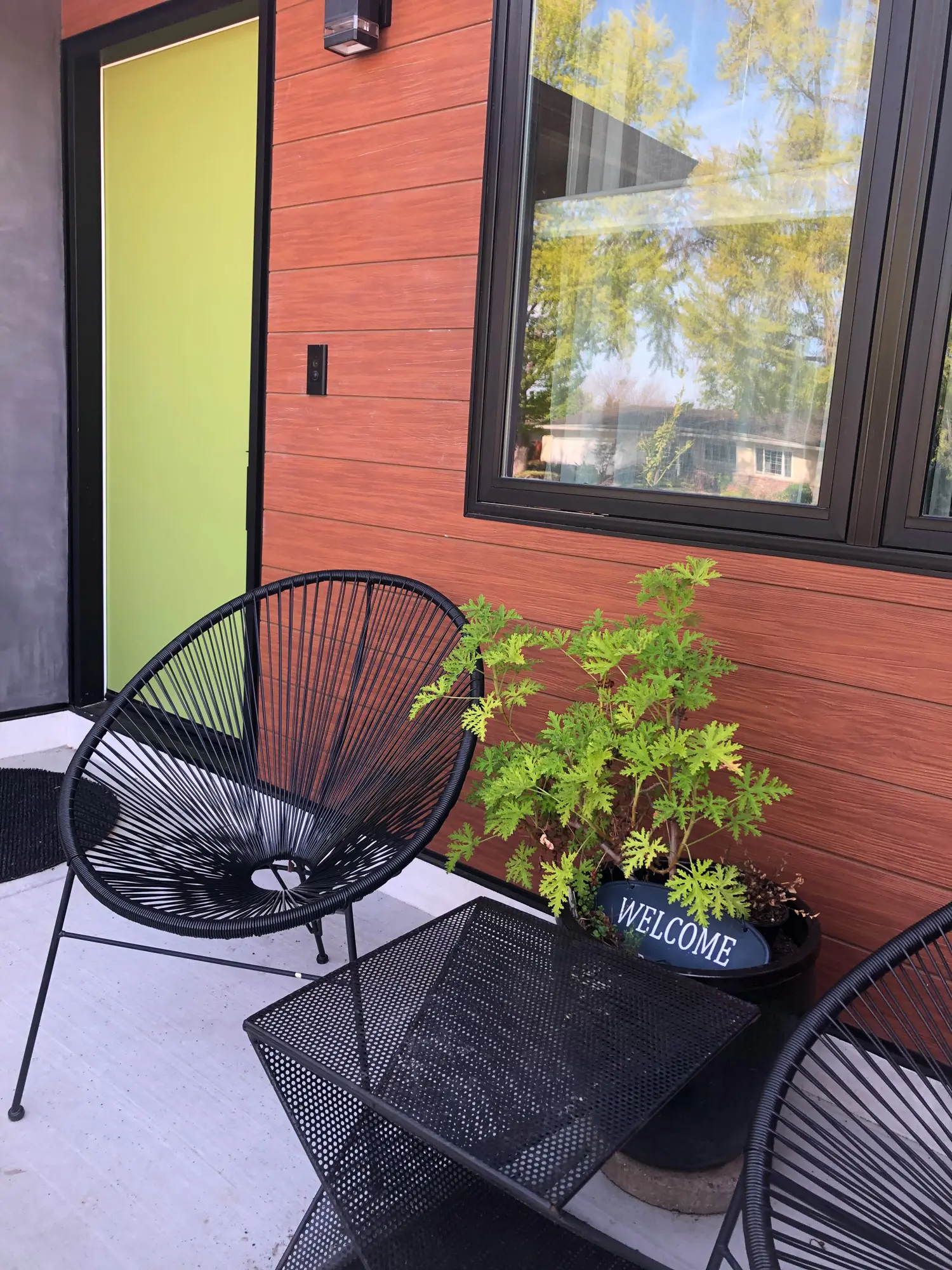 Modern front porch with wood siding, lime green door, and black wire chairs