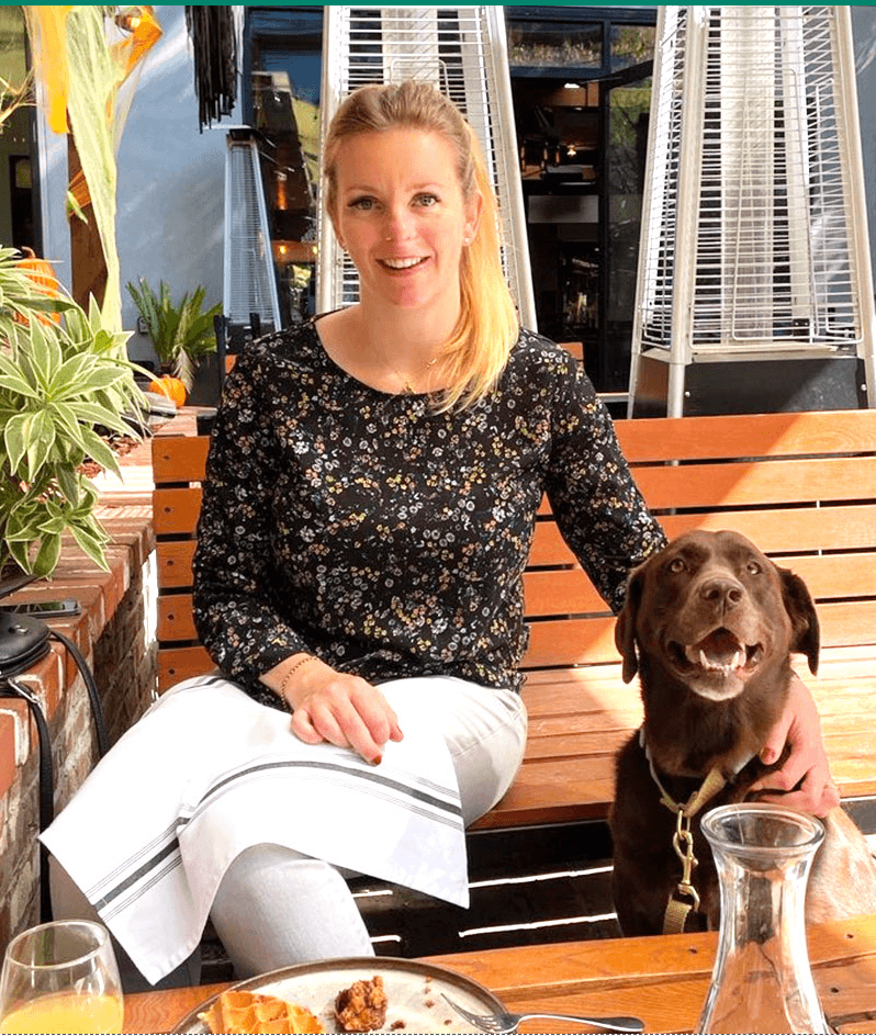 Michelle Johnson and Daisy Smiling interior design client sitting on a bench with her hand on a medium sized dog, both looking at the camera.
