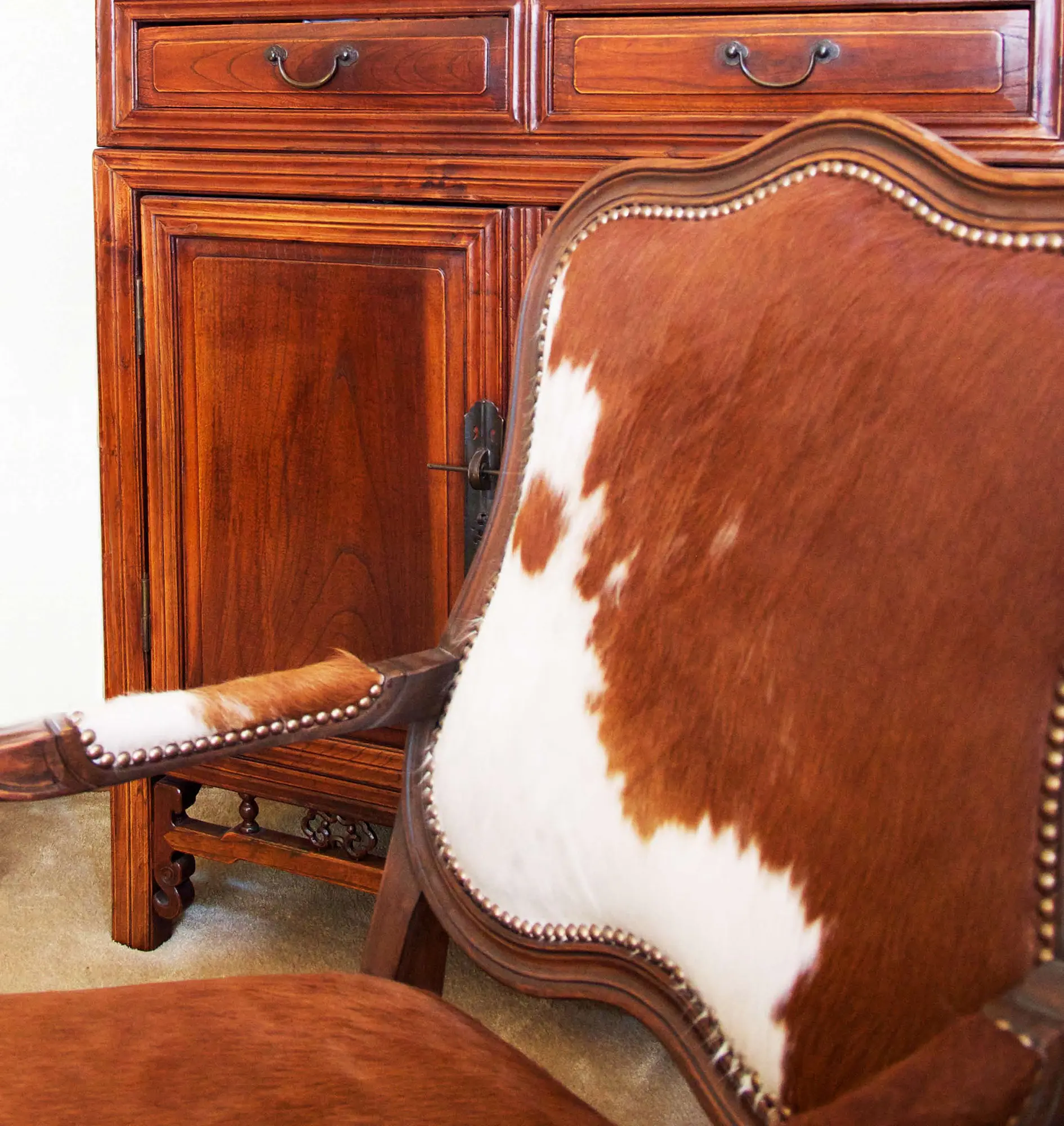 Cowhide accent chair beside richly stained traditional wood cabinet