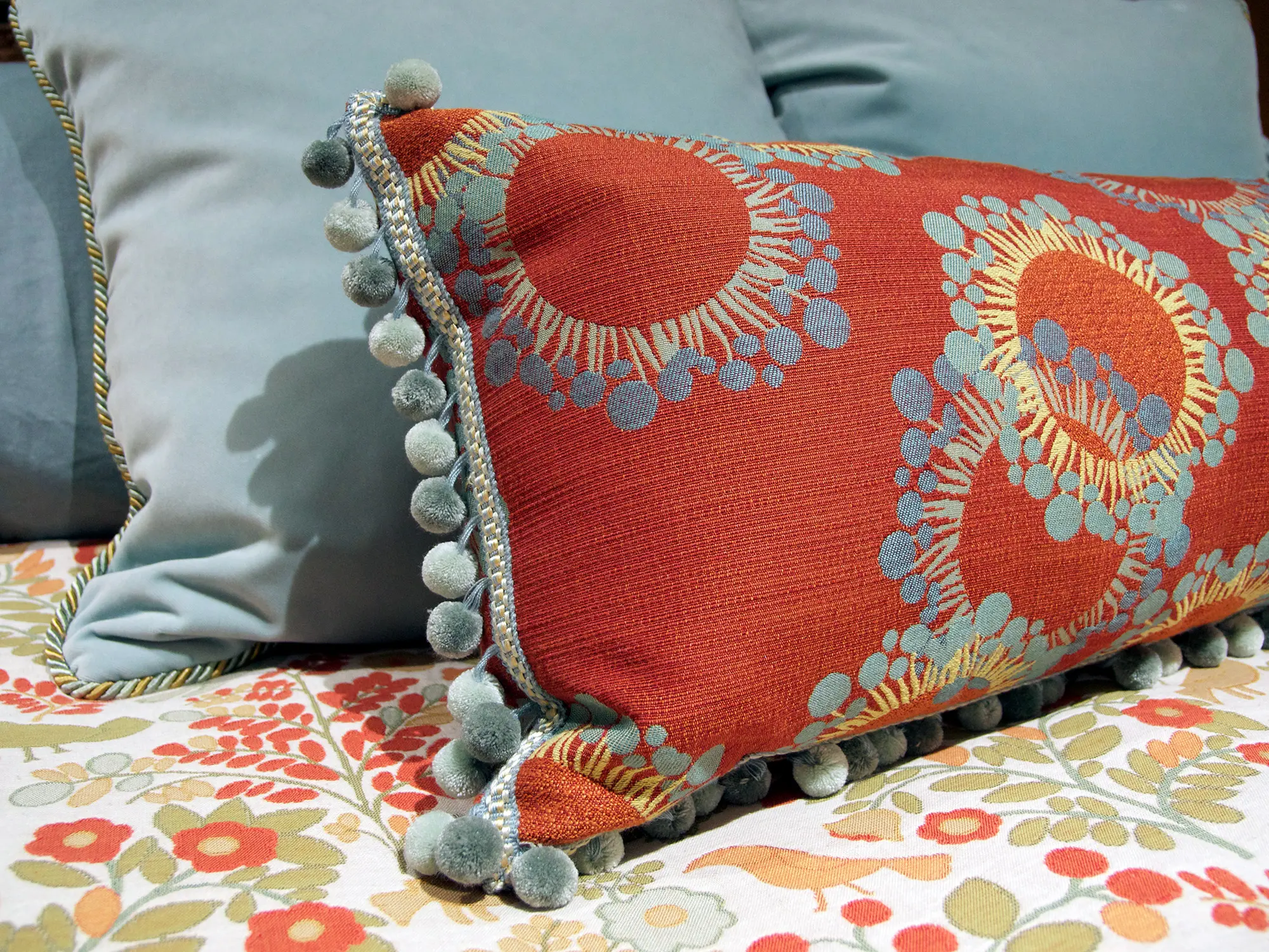 Close-up of colorful designer pillows with pom-pom trim on floral bedding