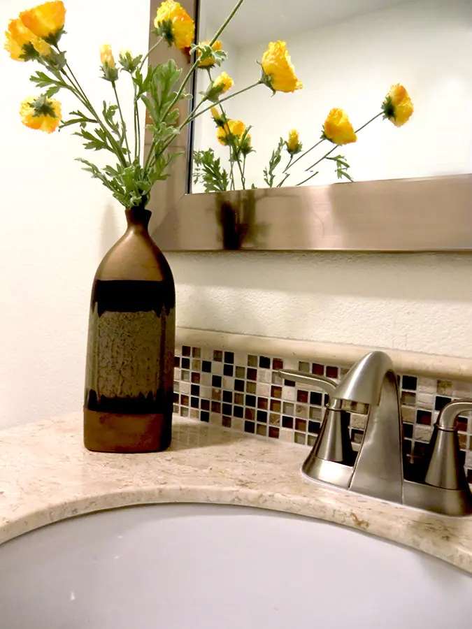 Bathroom vanity close-up with mosaic tile backsplash, brushed nickel faucet, and floral styling